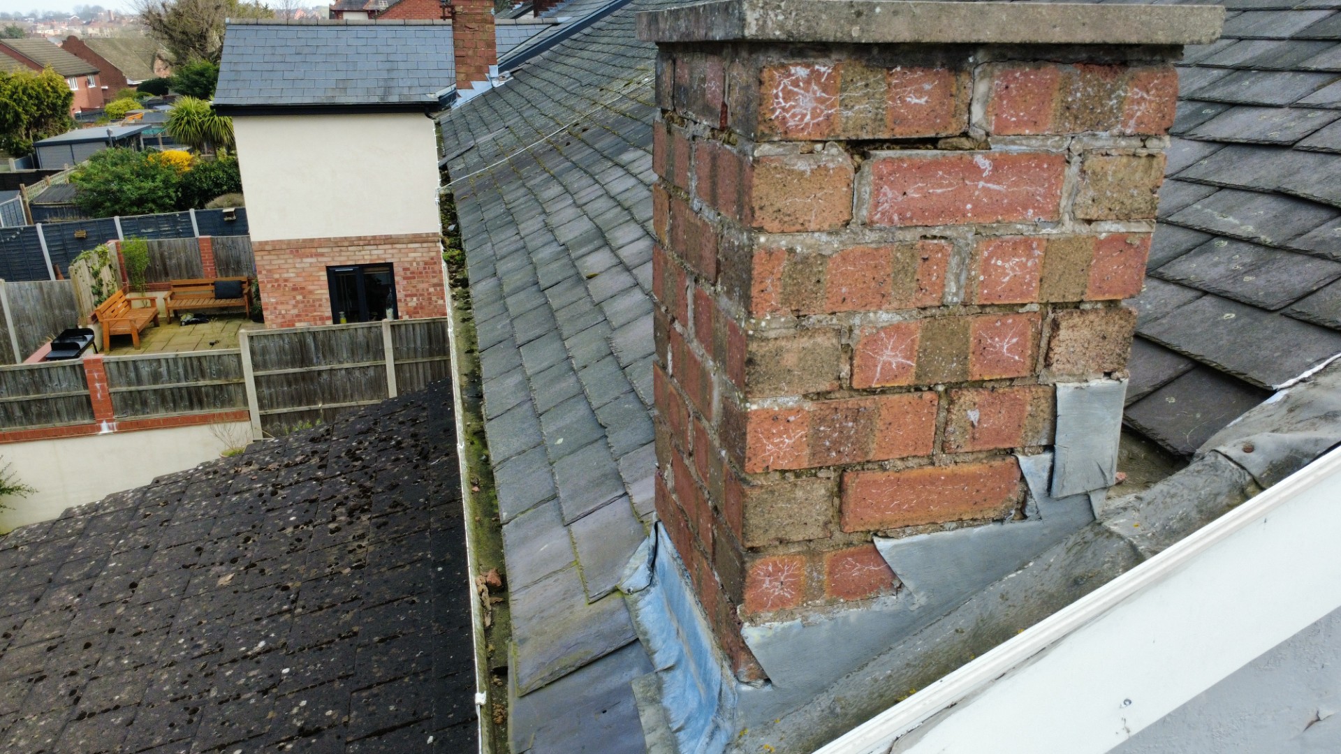 Close aerial view of a chimney stack with cracked, spalled brickwork and patched lead flashing